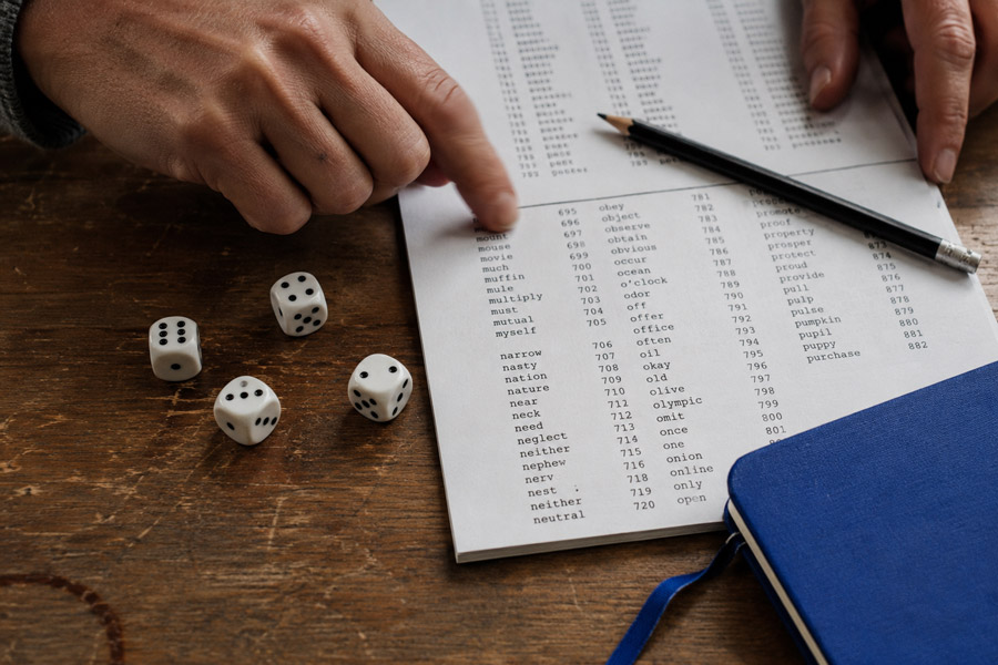 Hands using dice and a printed word list to select random words for a passphrase.