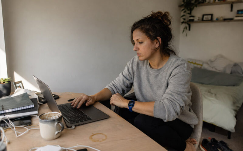 Woman working at a home desk while her smartwatch displays an ignored stand-up reminder.