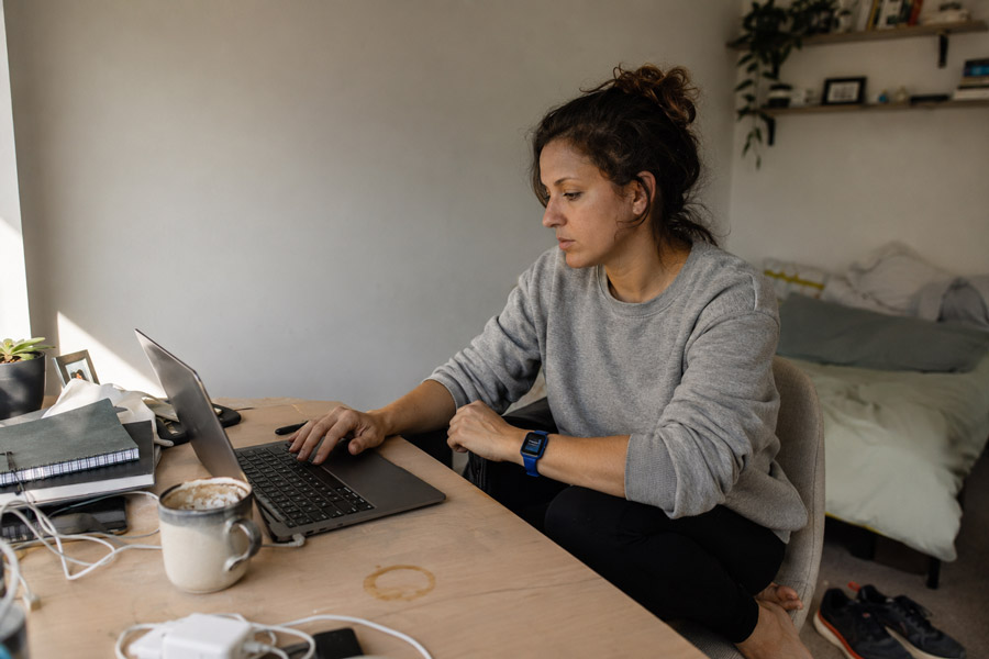 Woman working at a home desk while her smartwatch displays an ignored stand-up reminder.
